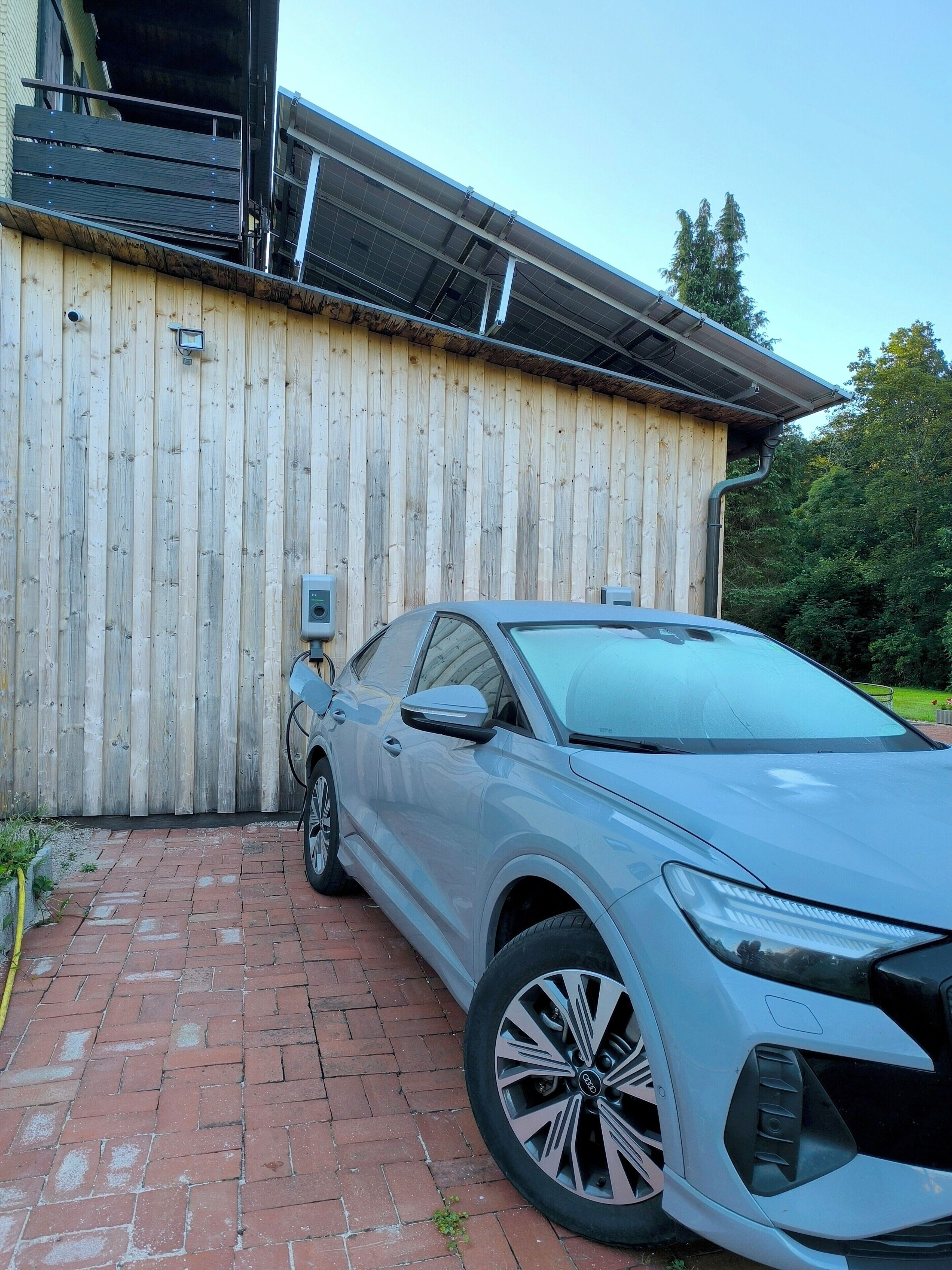 Un coche plateado estacionado frente a un edificio de madera con un panel solar en el techo.