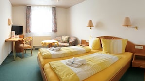 A hotel room with two beds, a desk, a chair, a TV, and a window with curtains. - Hotel Adler - Post (Baiersbronn)