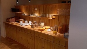 A breakfast bar with various food items and drinks, wooden cabinets, and shelves with glassware. - Hotel Adler - Post (Baiersbronn)