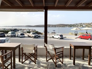 A covered outdoor seating area with tables and chairs, overlooking a marina with parked cars and boats.