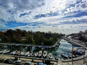 A marina with boats docked, a road leading to the marina, and a cityscape in the background. - Carol (Piraeus)