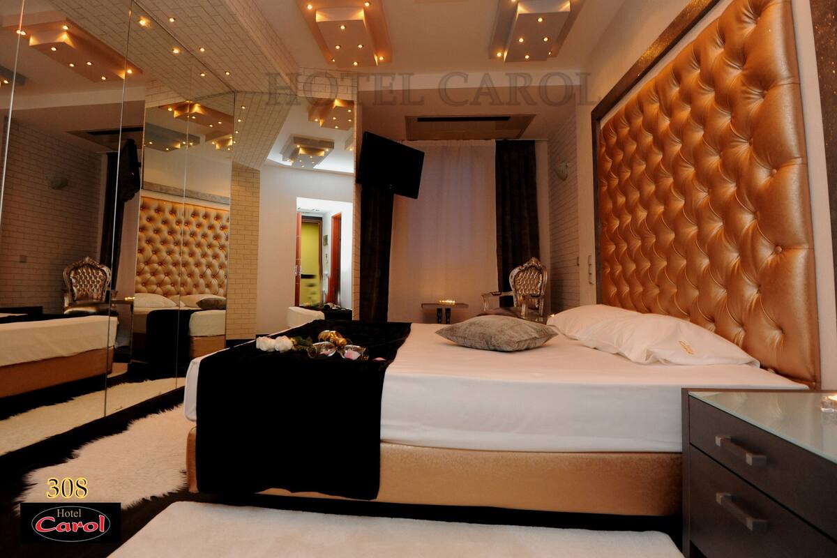 Una habitación de hotel moderna con una cama grande, un espejo, un cabecero capitonado y un tocador de vidrio.