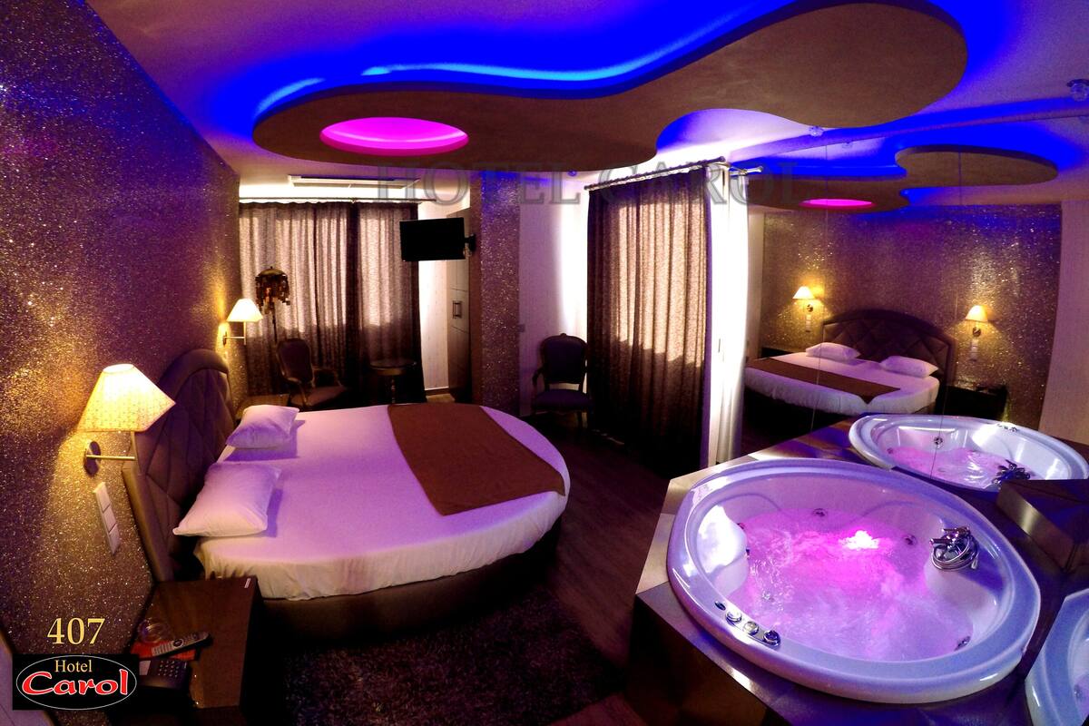 Una habitación de hotel con una cama grande, dos camas individuales, una zona de estar, un televisor y dos jacuzzis.
