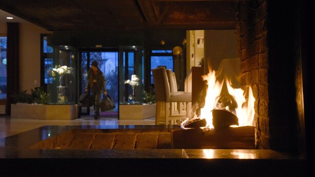 A fireplace with a fire, a glass door, and a person walking in the background.