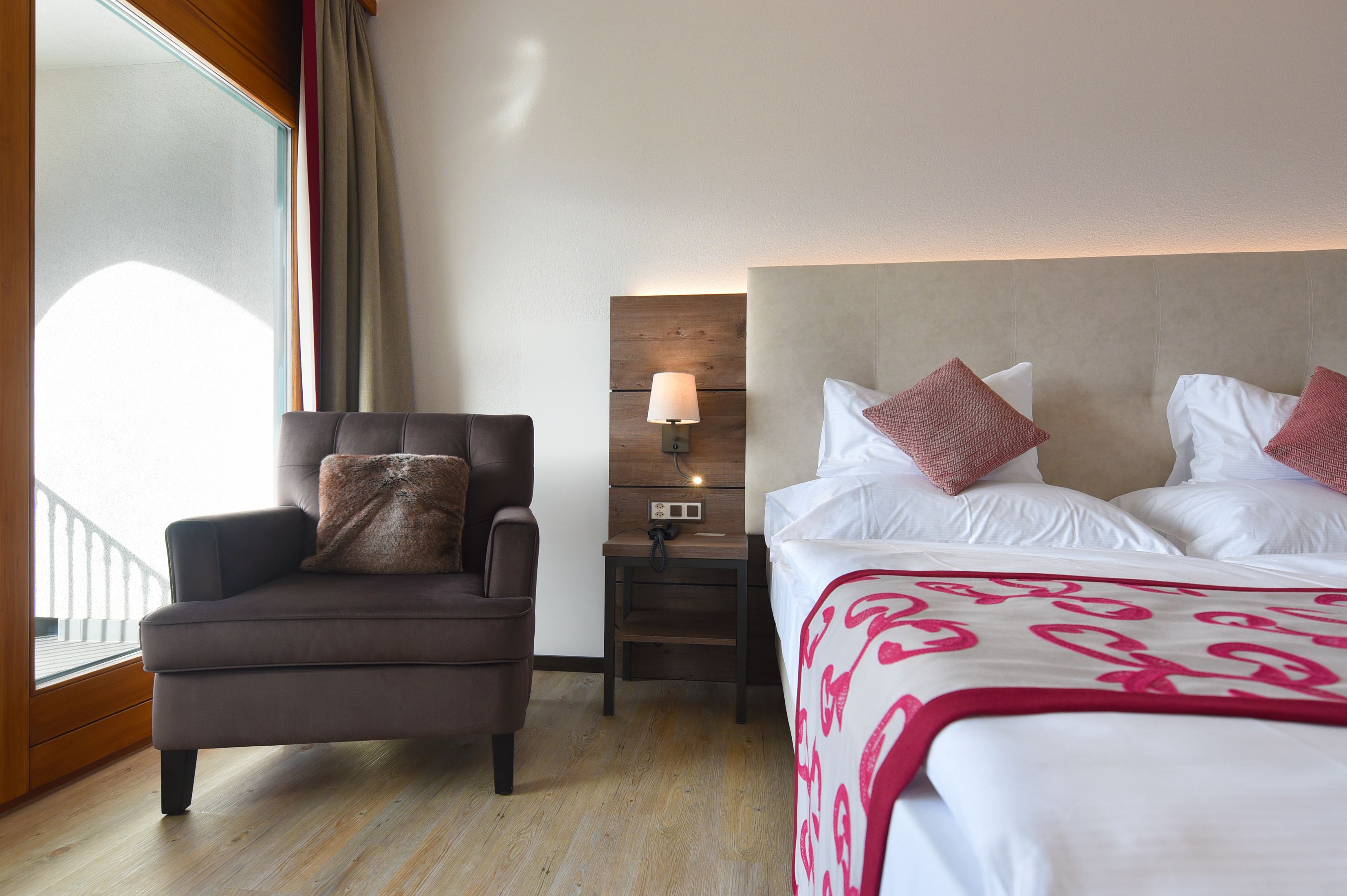 Ein Hotelzimmer mit Bett, Stuhl, Nachttisch mit Lampe und einem Fenster mit Vorhängen.