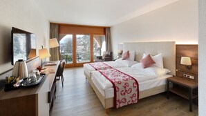 A hotel room with a large bed, a desk with a lamp, a chair, and a view of the outdoors through a sliding door.