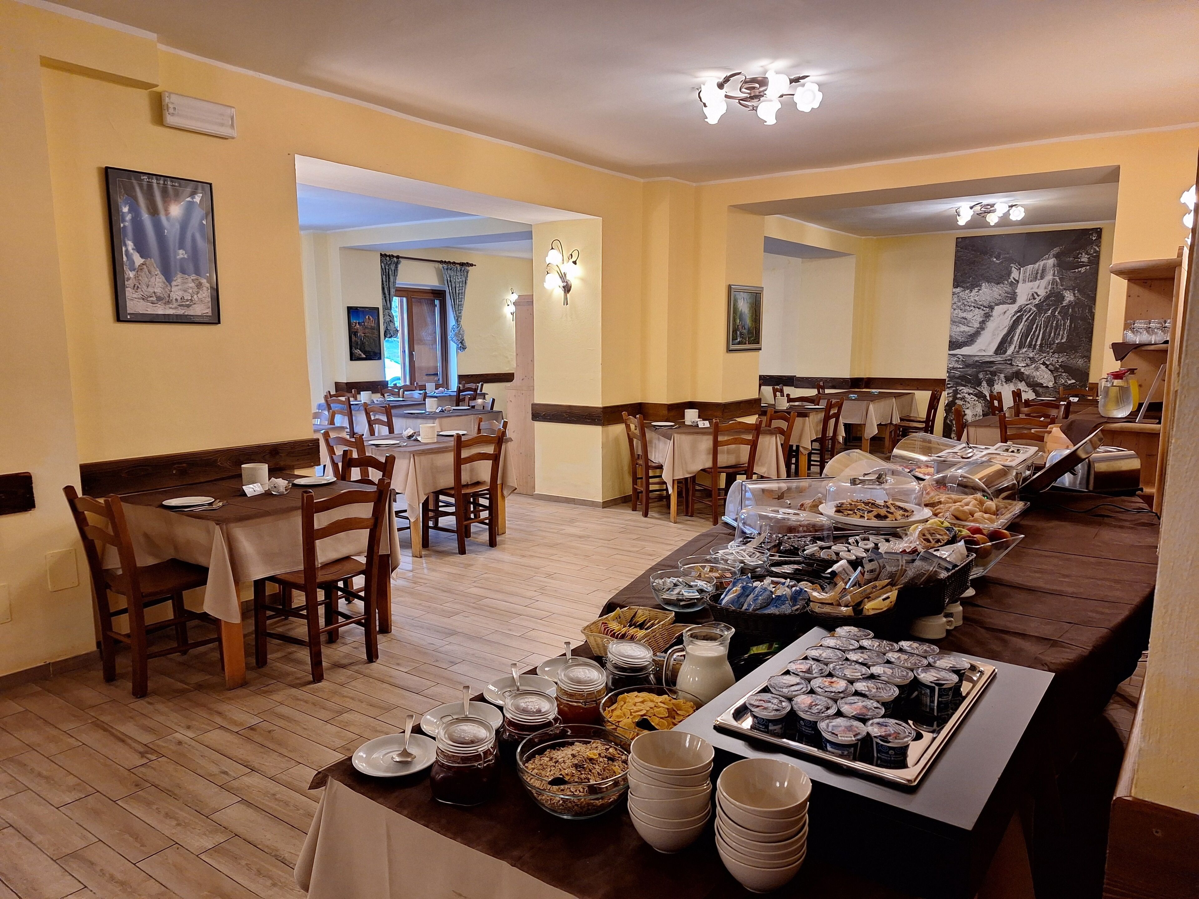 A dining area with multiple tables and chairs, a buffet with various food items, and artwork on the walls.