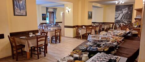 A dining area with multiple tables and chairs, a buffet with various food items, and artwork on the walls.