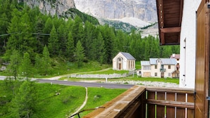 Une vue sur la montagne, avec un mur de pierre, une petite chapelle et une route menant à un bâtiment doté d’un toit en métal.