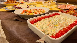 Une table de buffet proposant divers plats, dont un grand plat de service contenant une préparation agrémentée de tomates cerises.