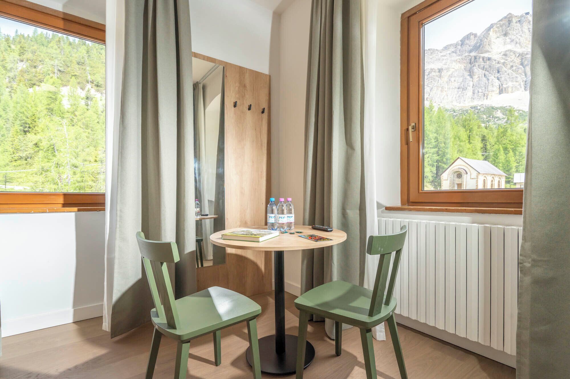 A room with a round table, two chairs, a window with a view of mountains, and a radiator.