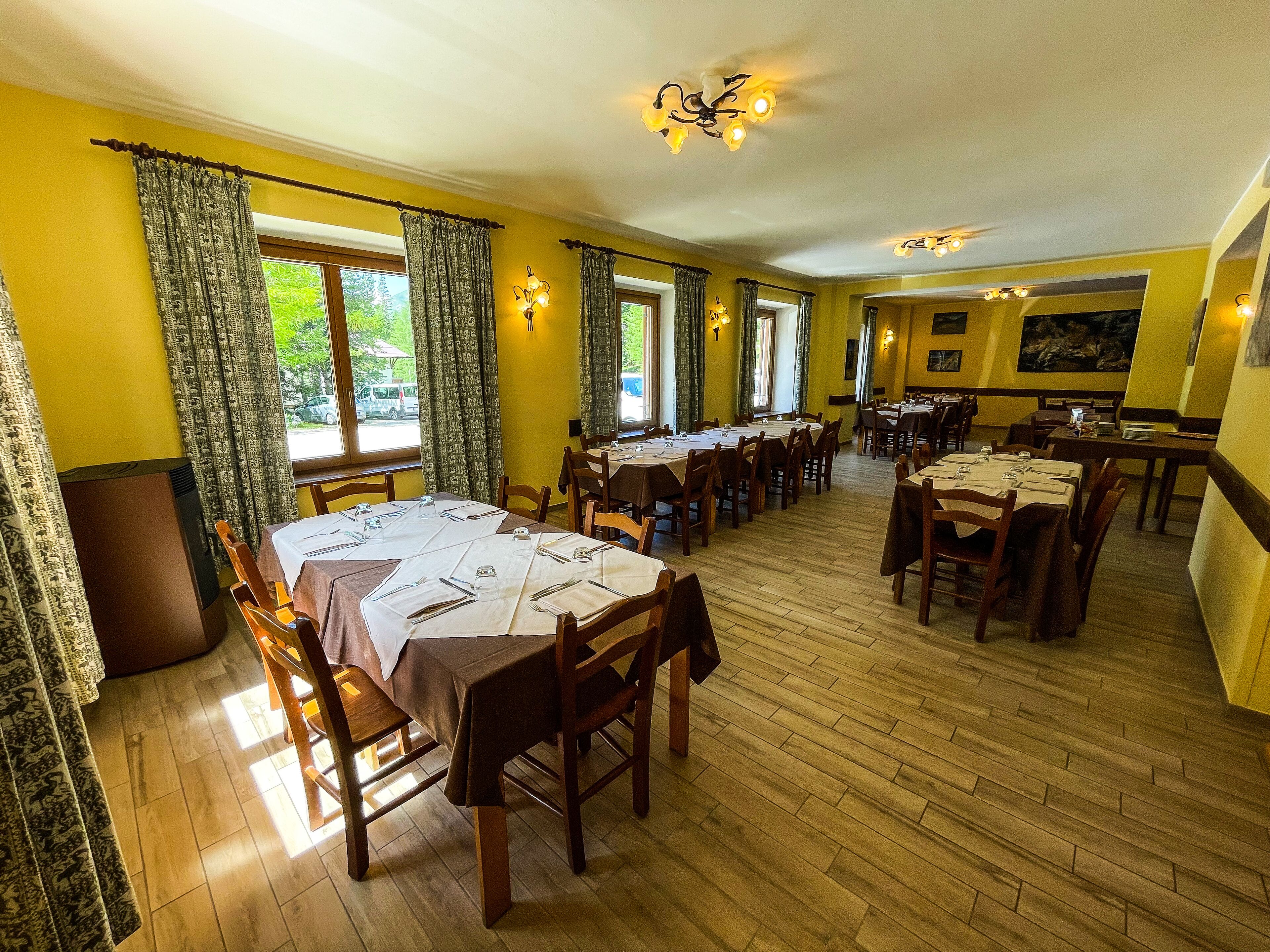 A dining area with multiple tables set for service, wooden flooring, and large windows allowing natural light.