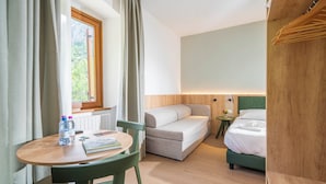 Une chambre d’hôtel avec un lit, une petite table sur laquelle se trouvent un livre et des bouteilles d’eau, une chaise et une fenêtre avec des rideaux.