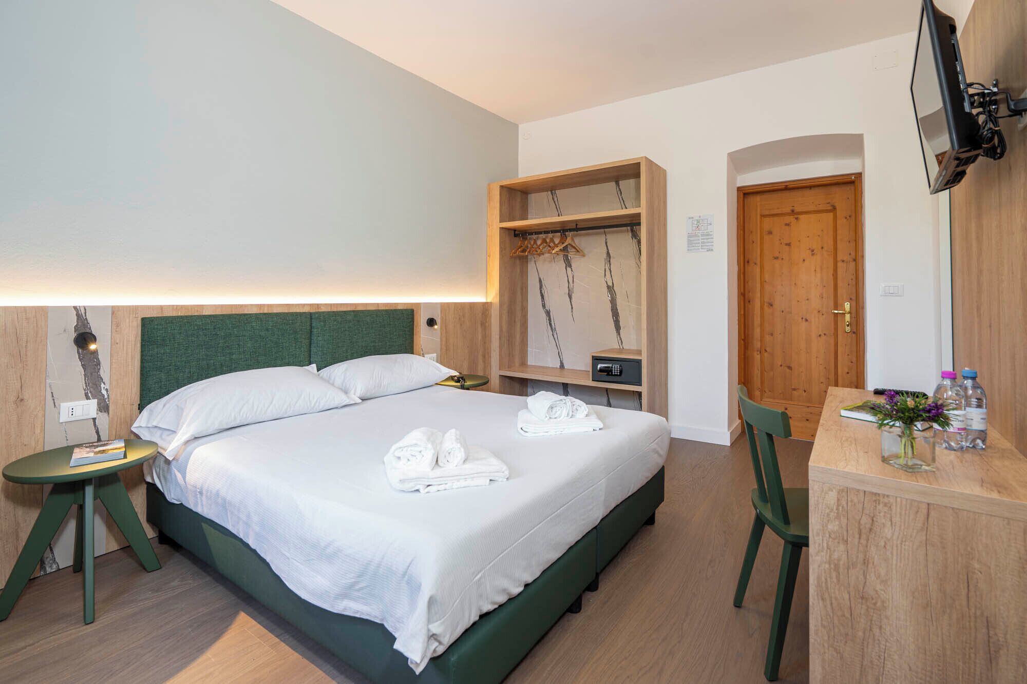 A hotel room with a bed, a desk, a chair, a TV mounted on the wall, and a wooden door.
