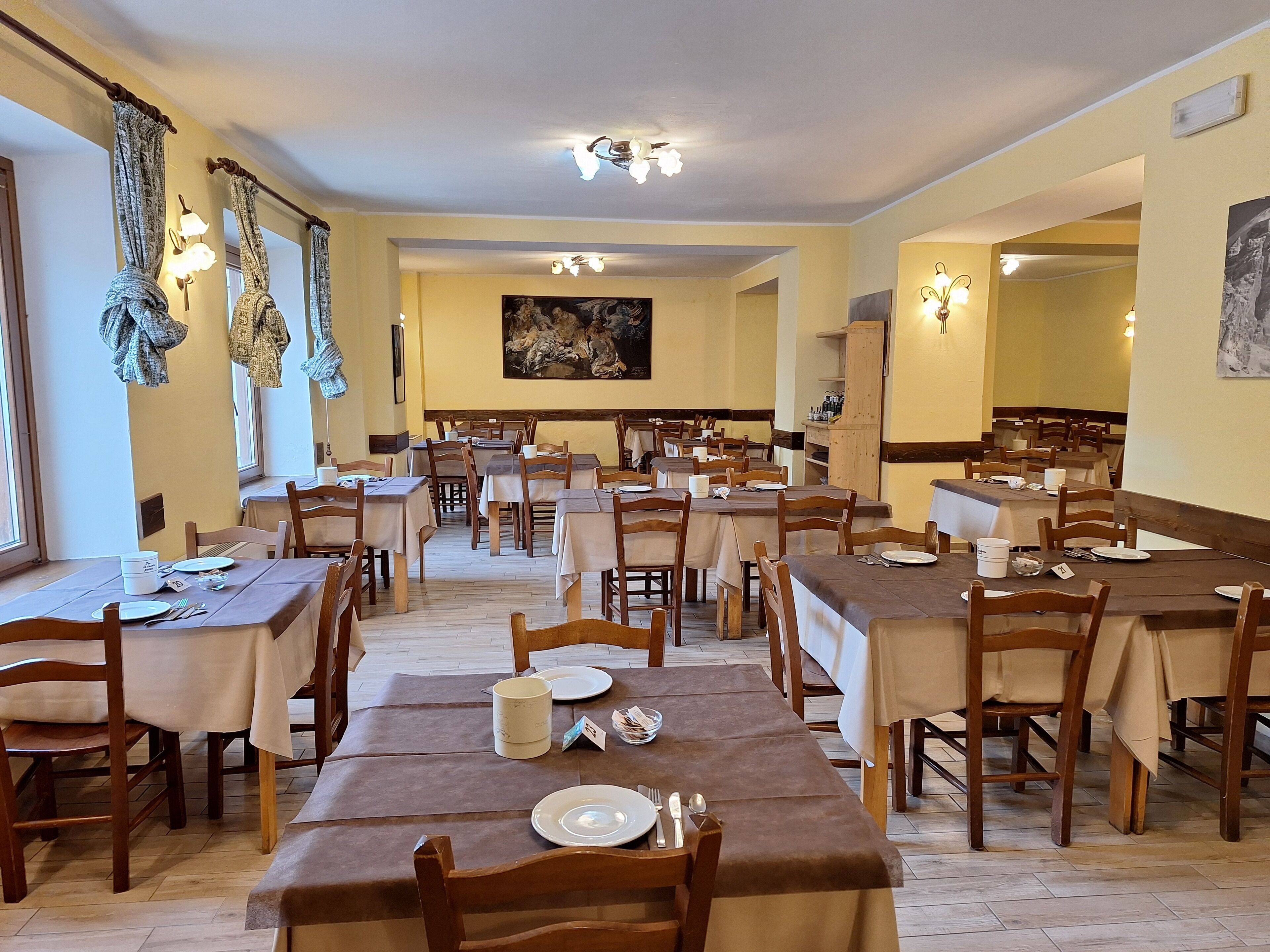 Un'area pranzo con diversi tavoli e sedie, pavimenti in legno e lampade a parete.