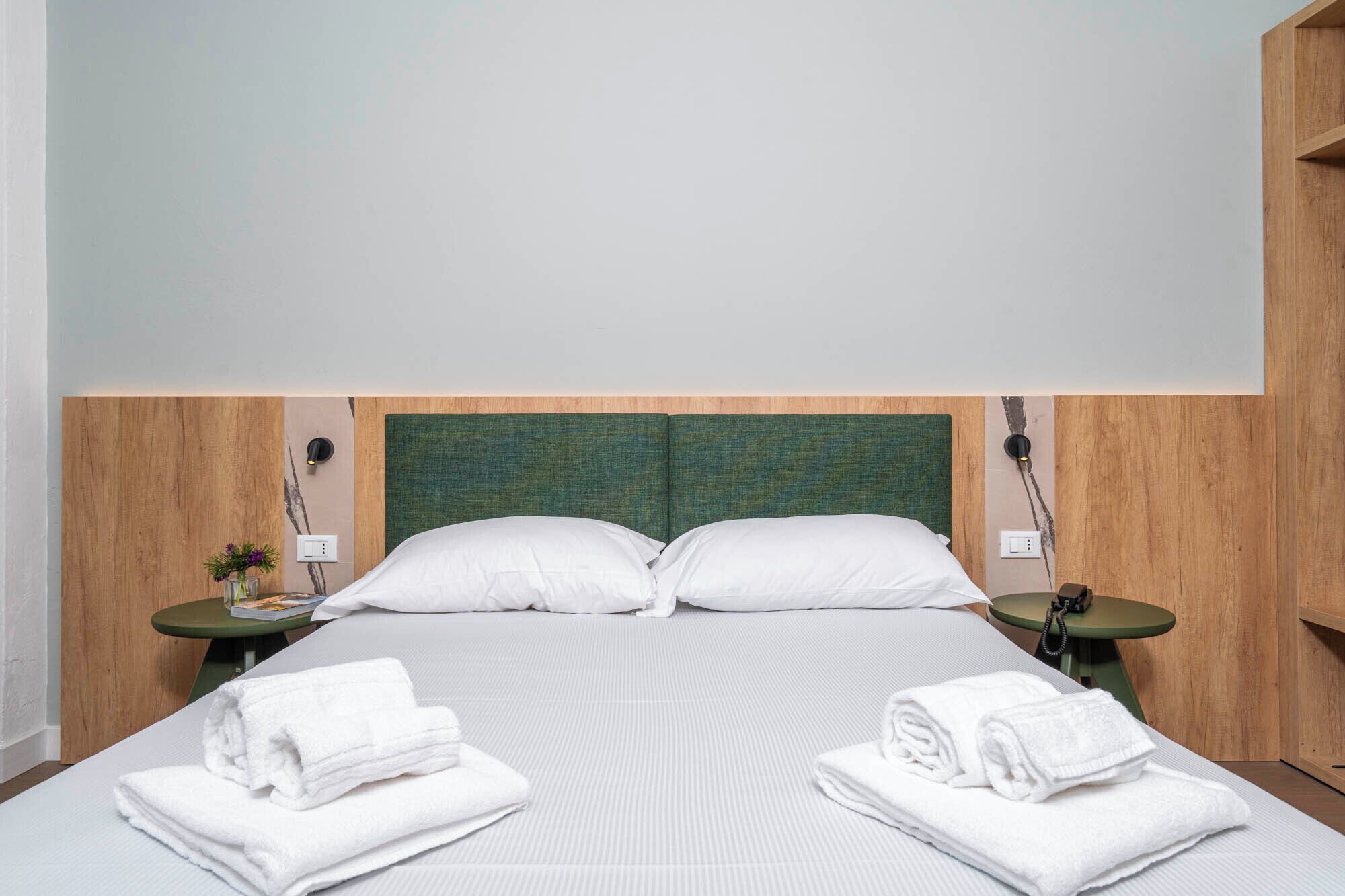 A hotel room with a large bed, two nightstands, and a green headboard.