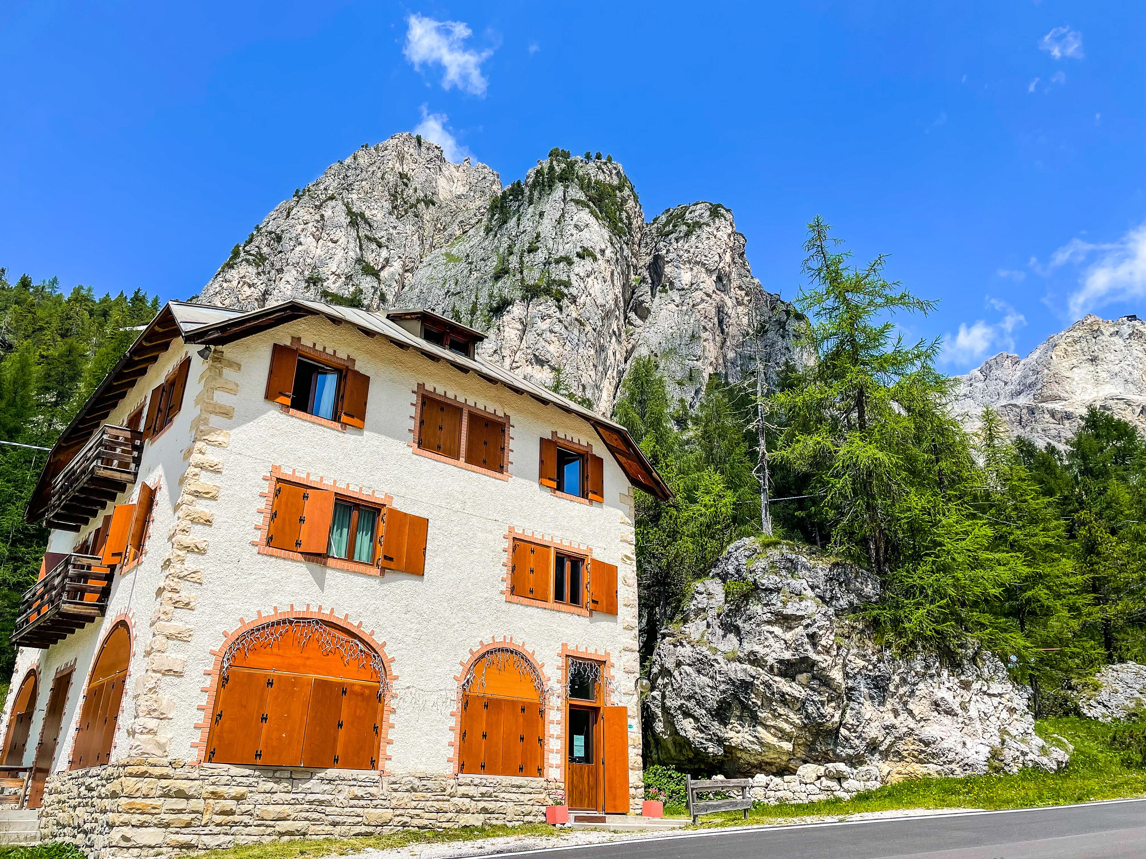 A stone building with wooden shutters and balconies, set against a mountainous backdrop.
