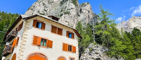 Ein Steinhaus mit Holzhörnern und Balkonen vor einer Bergkulisse.