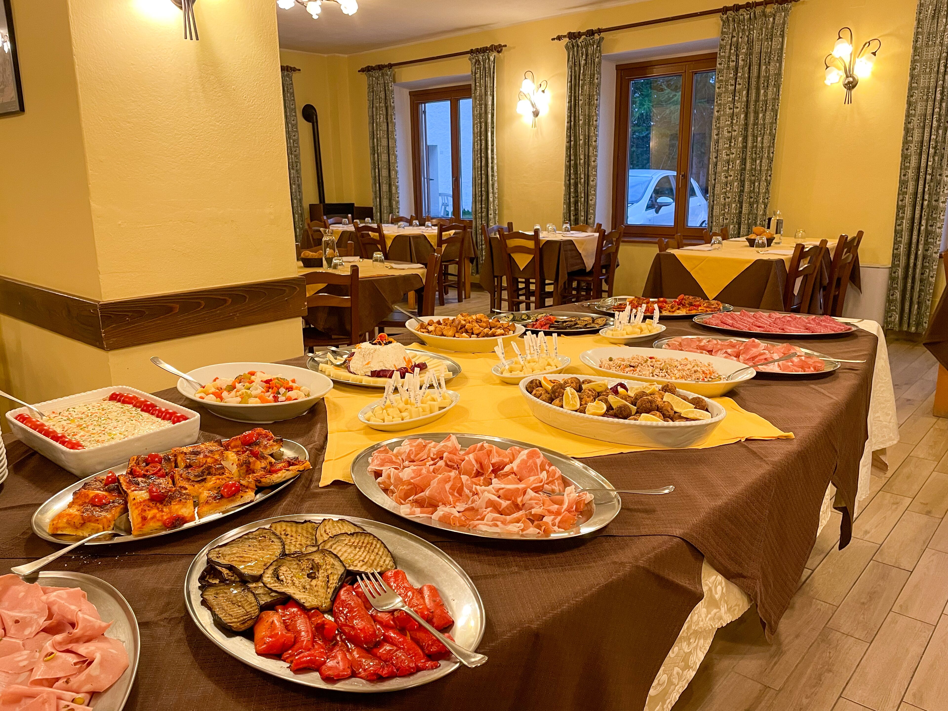 Ein reichhaltiges Buffet mit verschiedenen Speisen, darunter Fleisch, Käse und Gemüse, in einem Essbereich mit mehreren Tischen und Stühlen.