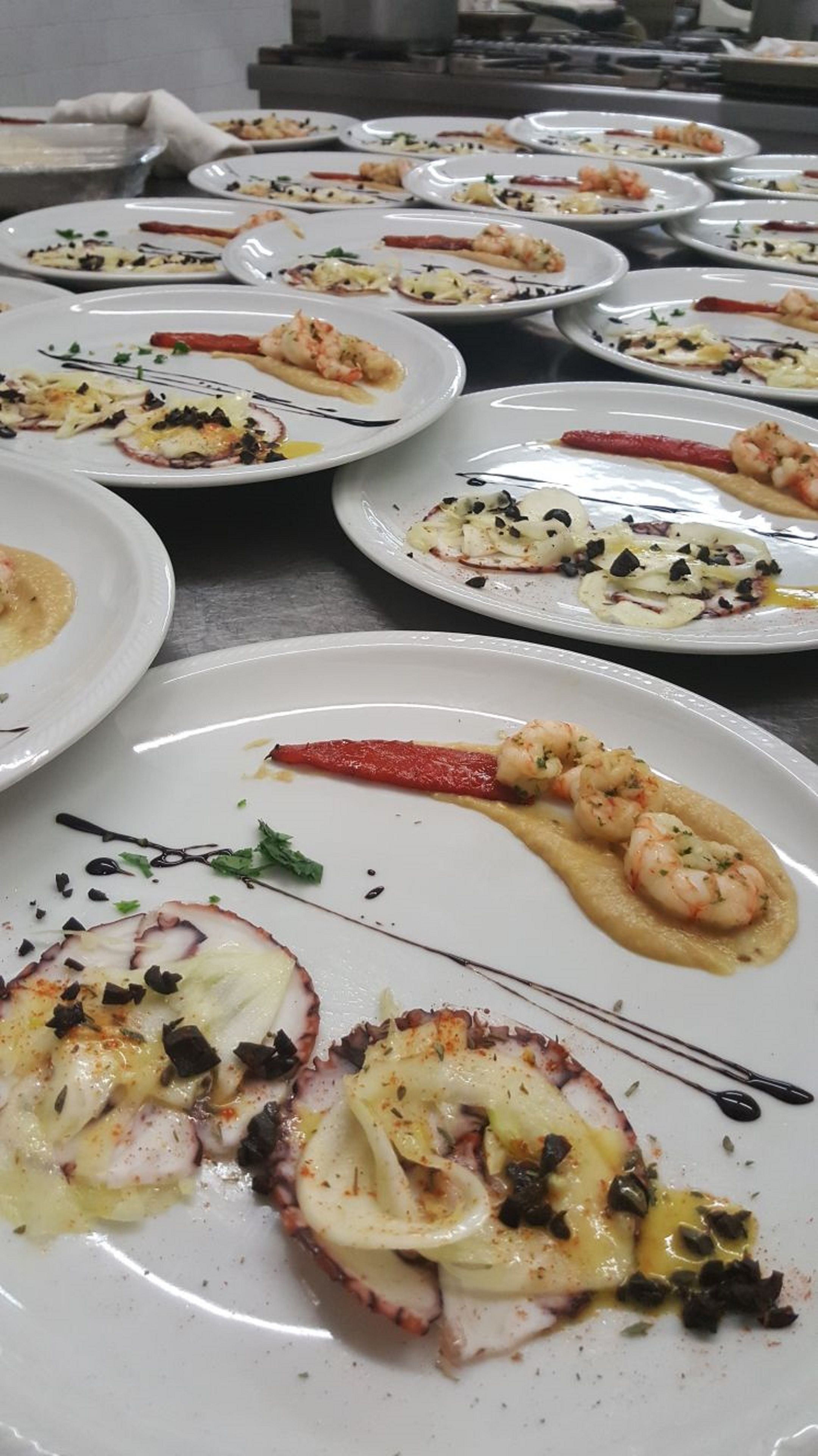 Verschiedene Meeresfrüchtegerichte auf weißen Tellern, darunter Garnelen und Tintenfisch, angerichtet auf einem Tisch.