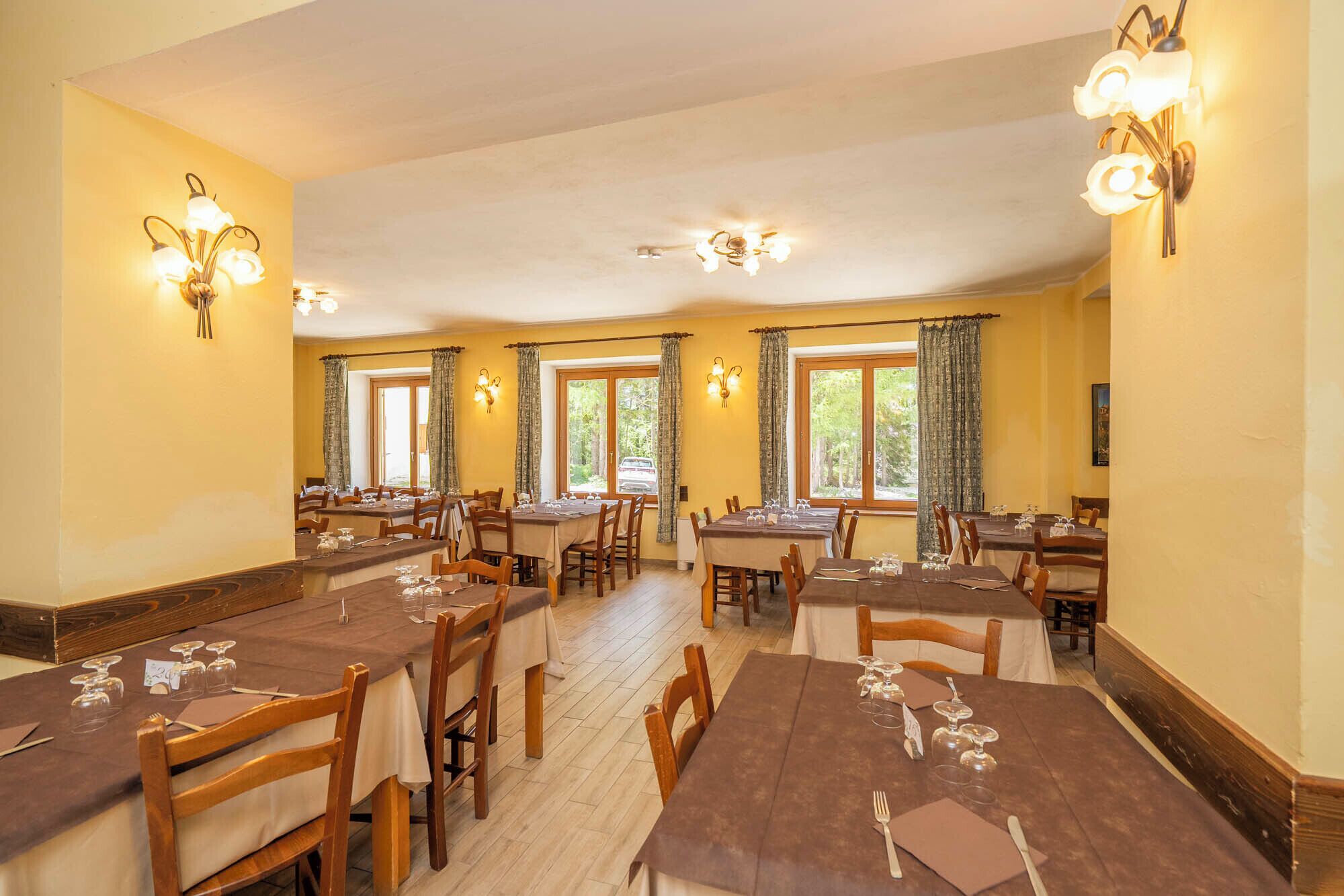 A dining area with multiple tables and chairs, light fixtures, and large windows.