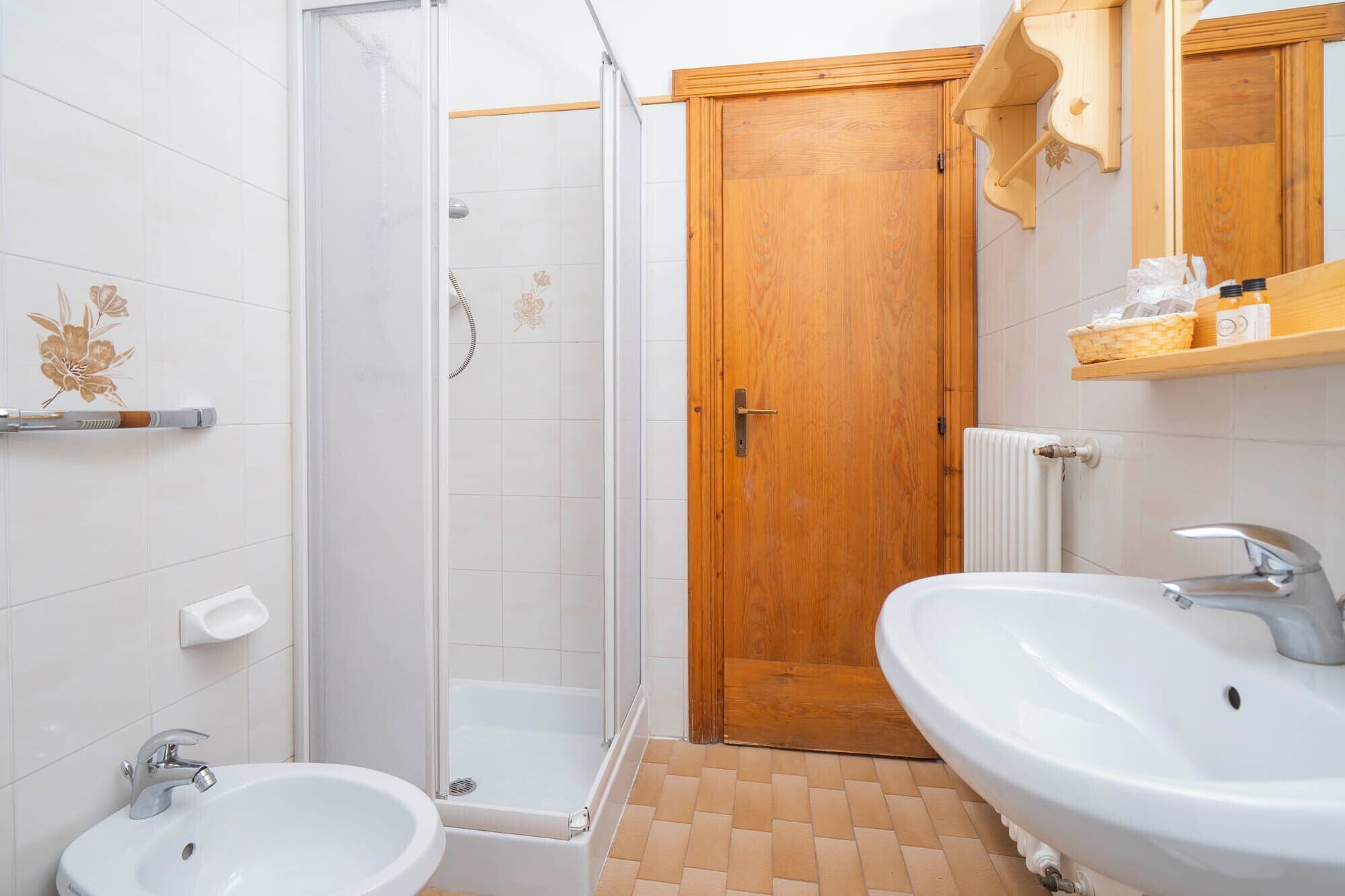 A bathroom with a shower, two sinks, a wooden door, and a radiator.