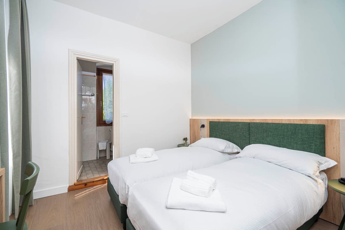 Une chambre d’hôtel avec deux lits, une tête de lit en bois, une petite table de chevet et un espace douche.