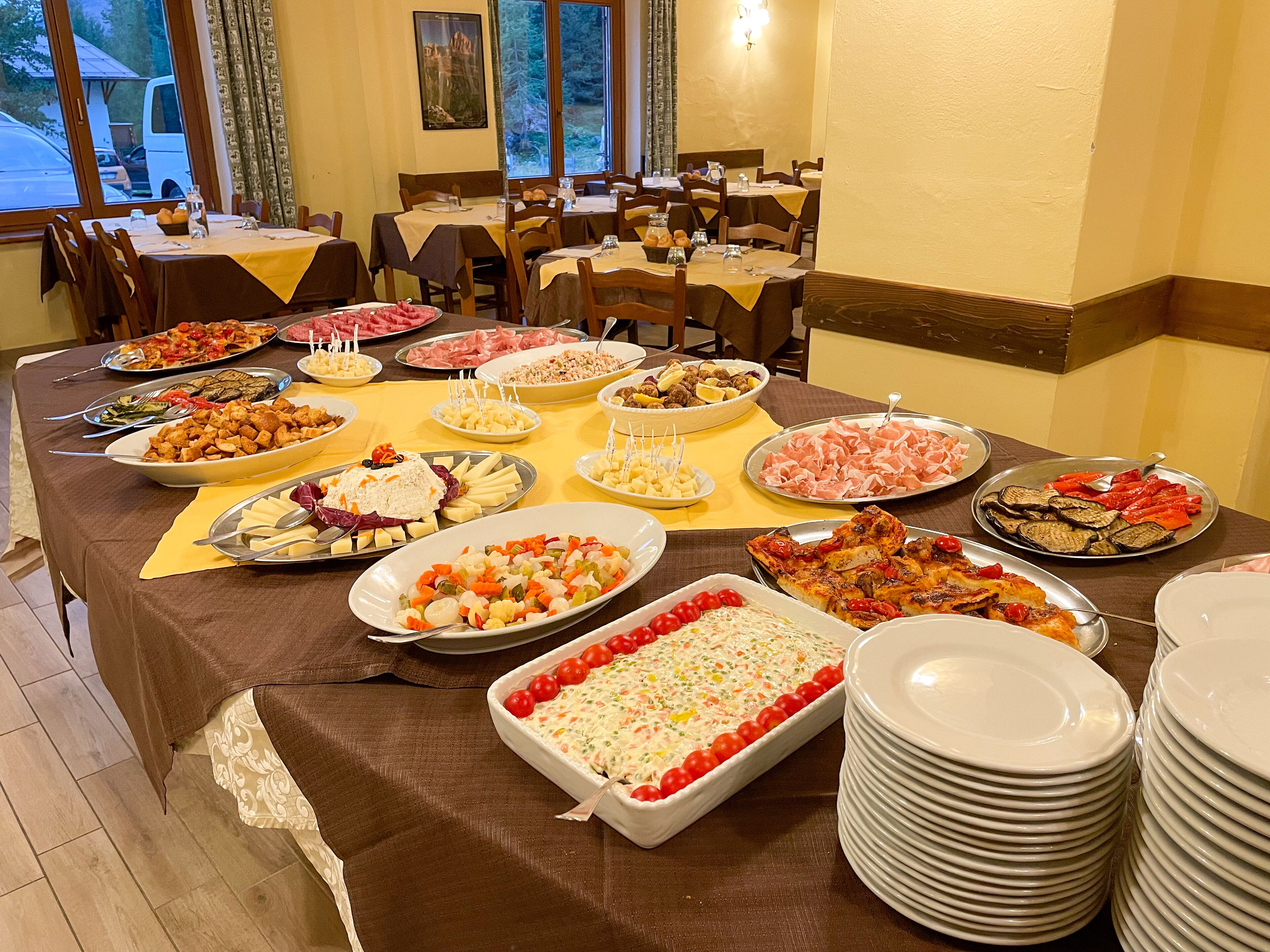 A buffet table with various dishes, including salads, meats, and desserts, in a dining area with tables and chairs.