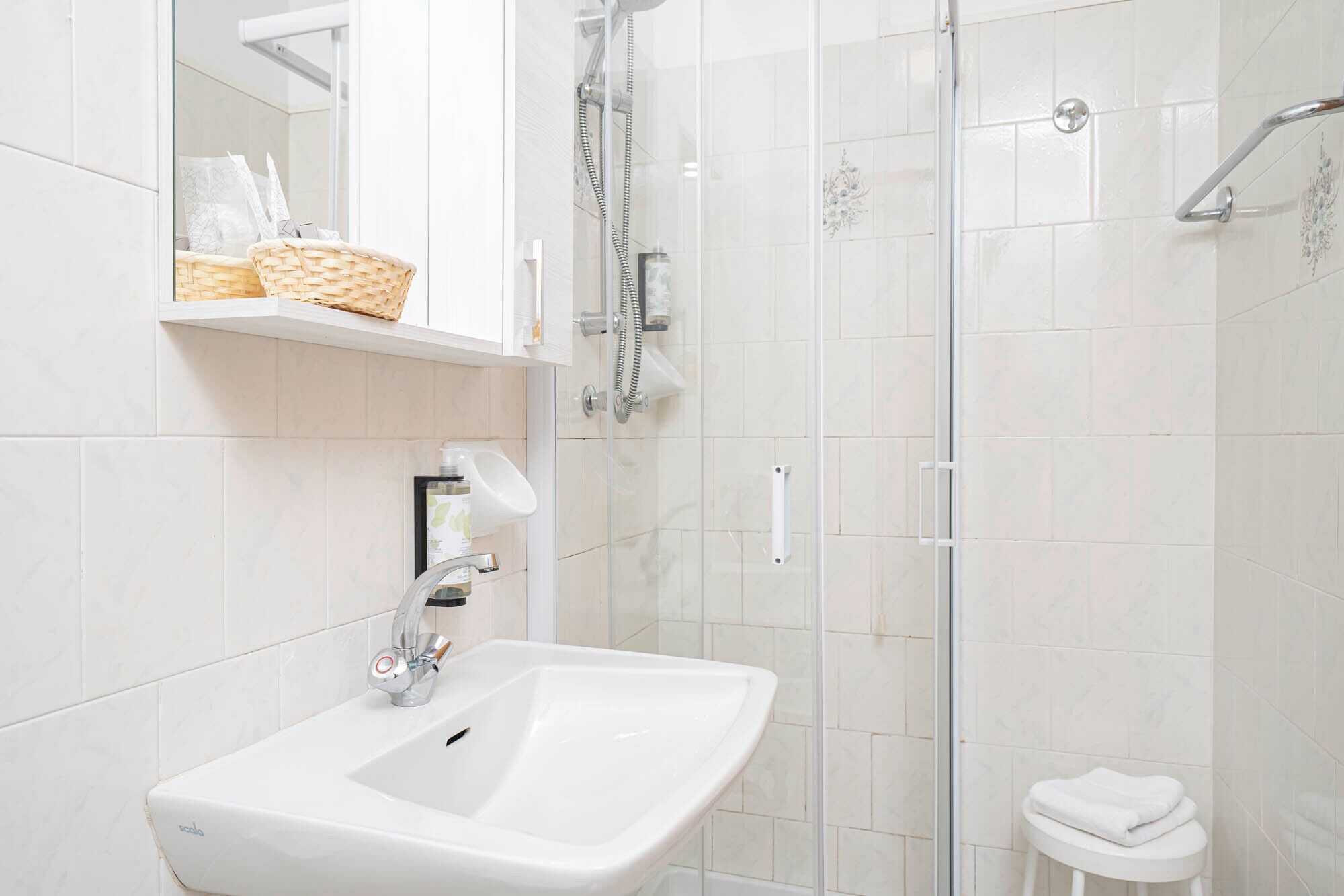 A modern bathroom with a white sink, a glass shower enclosure, and a small white stool.