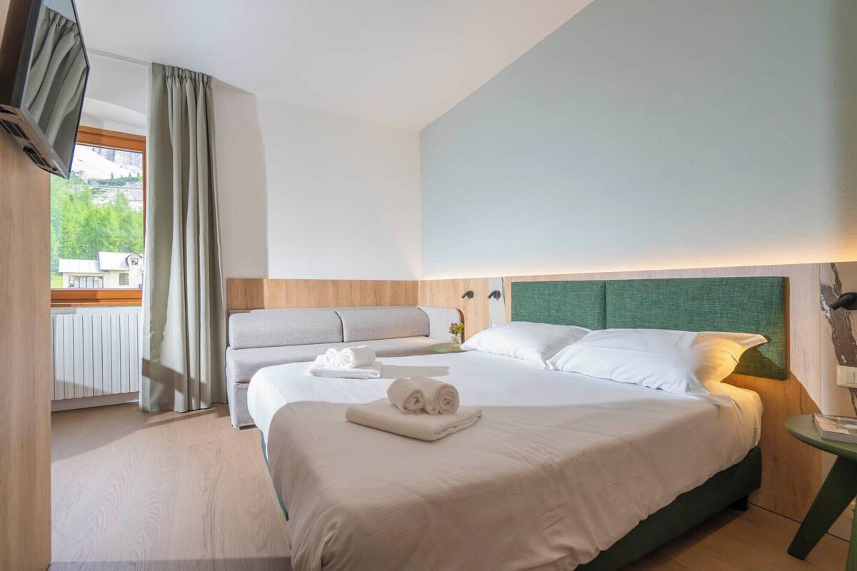 Une chambre d’hôtel avec deux lits, une vue sur l’extérieur et un mur d’accent de couleur verte.
