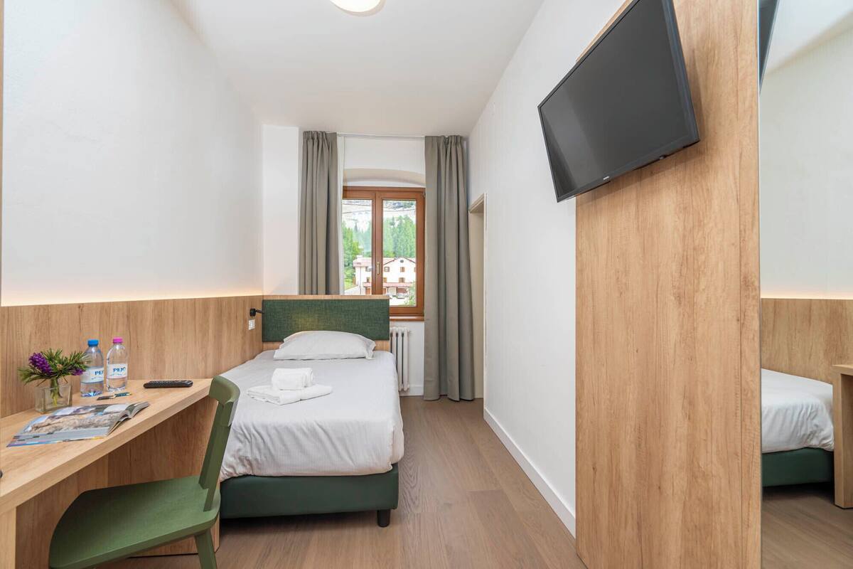 Une chambre d’hôtel comprenant un lit, un bureau avec une chaise, un téléviseur fixé au mur et une fenêtre avec des rideaux.
