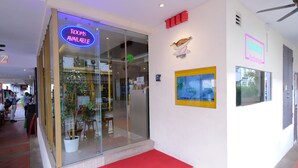 Fachada de hotel con un letrero de neón que indica habitaciones disponibles, un mural de aves y un mapa en la pared.