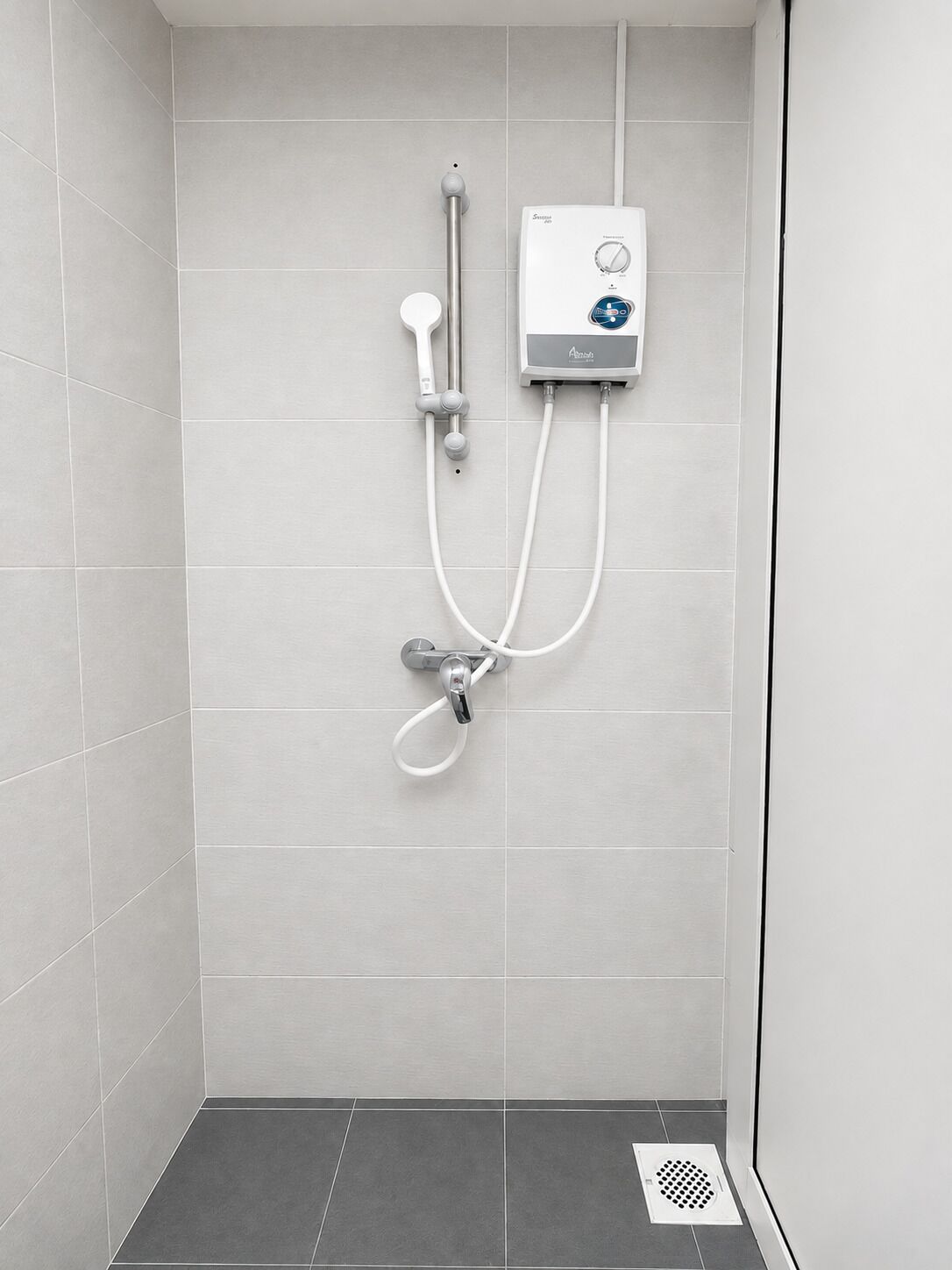 A shower with a control panel, a handheld showerhead, and a wall-mounted faucet.