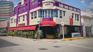 Un hotel con fachada morada y blanca, toldo rojo y entrada visible.