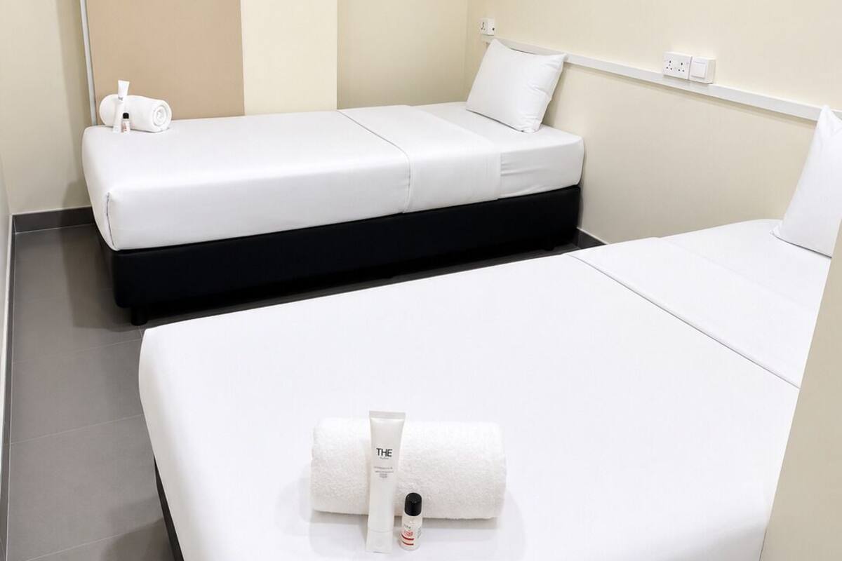 A hotel room with two beds, a flat-screen TV, a wall-mounted power outlet, and a towel on the floor.