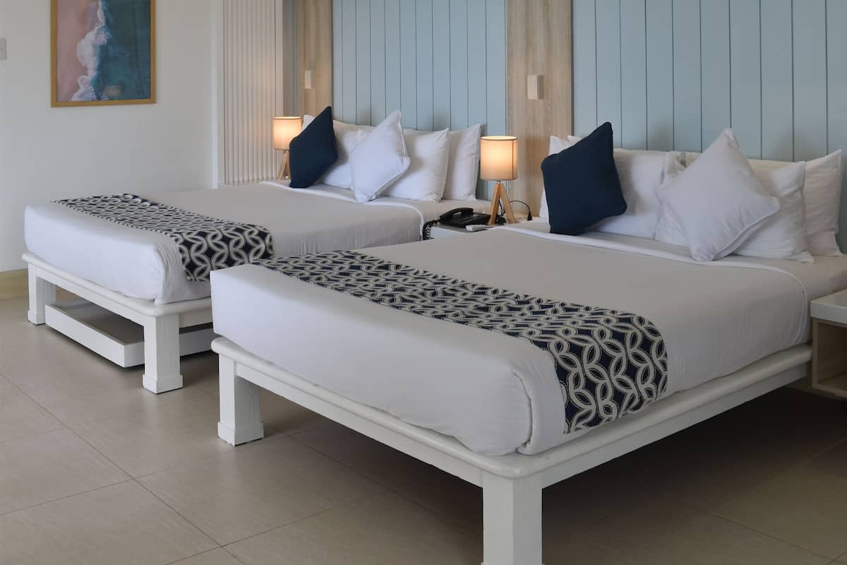 A hotel room with two beds, a large painting, and a ceiling with recessed lighting.