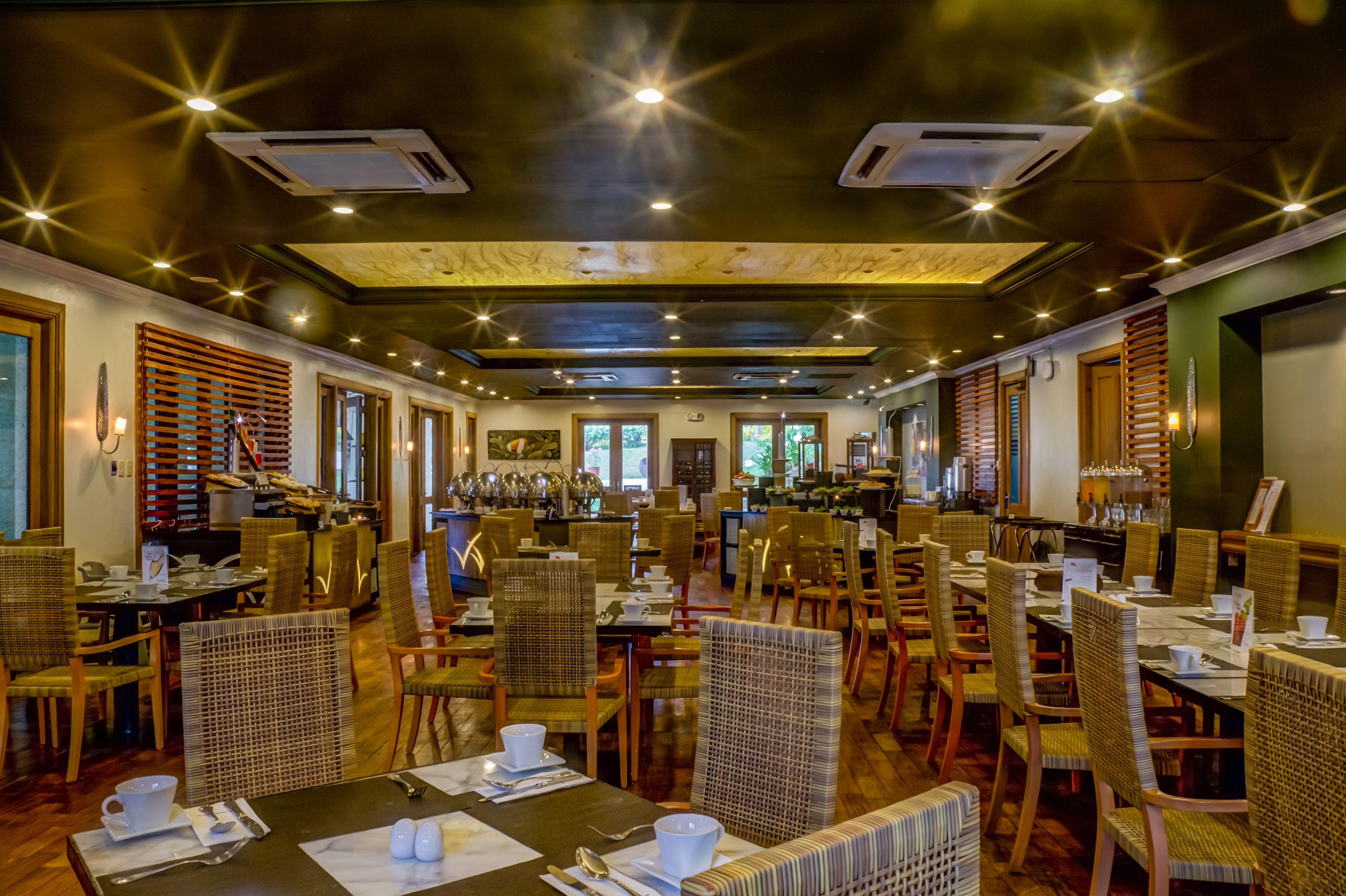 A restaurant with multiple dining tables and chairs, ceiling lights, and air conditioning units.