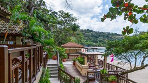 A wooden deck with a view of a beach and a building with a tiled roof. - Club Punta Fuego (Nasugbu)