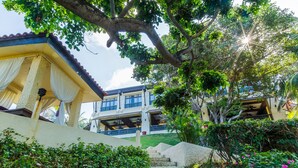 A building with a staircase leading to a balcony, surrounded by lush greenery and a tree. - Club Punta Fuego (Nasugbu)