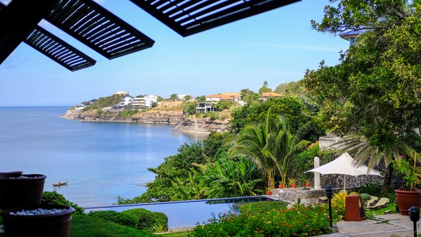 A coastal view with a swimming pool, lush greenery, and a clear sky. - Club Punta Fuego (Nasugbu)