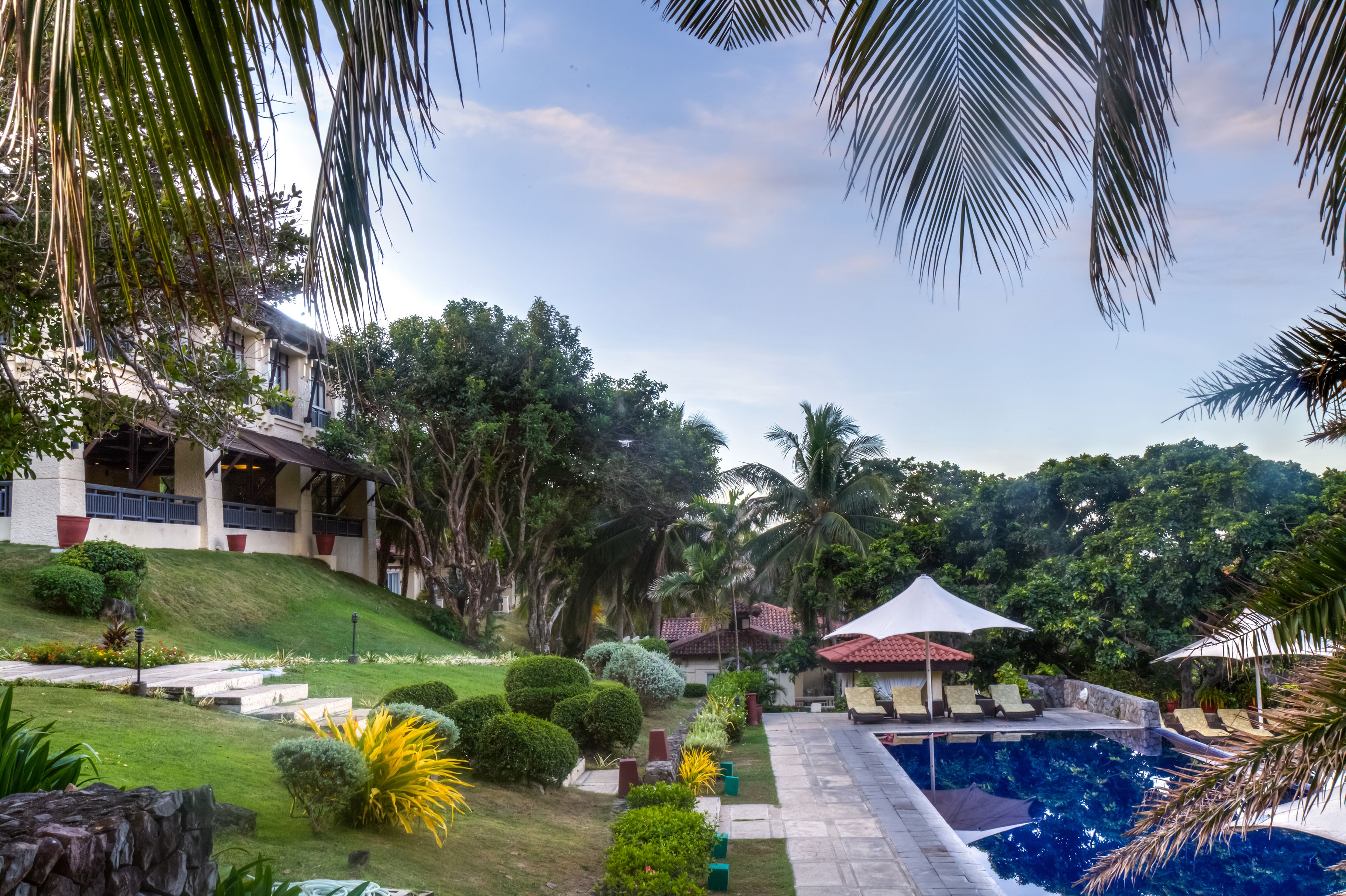 A resort with a swimming pool, lounge chairs, and palm trees.