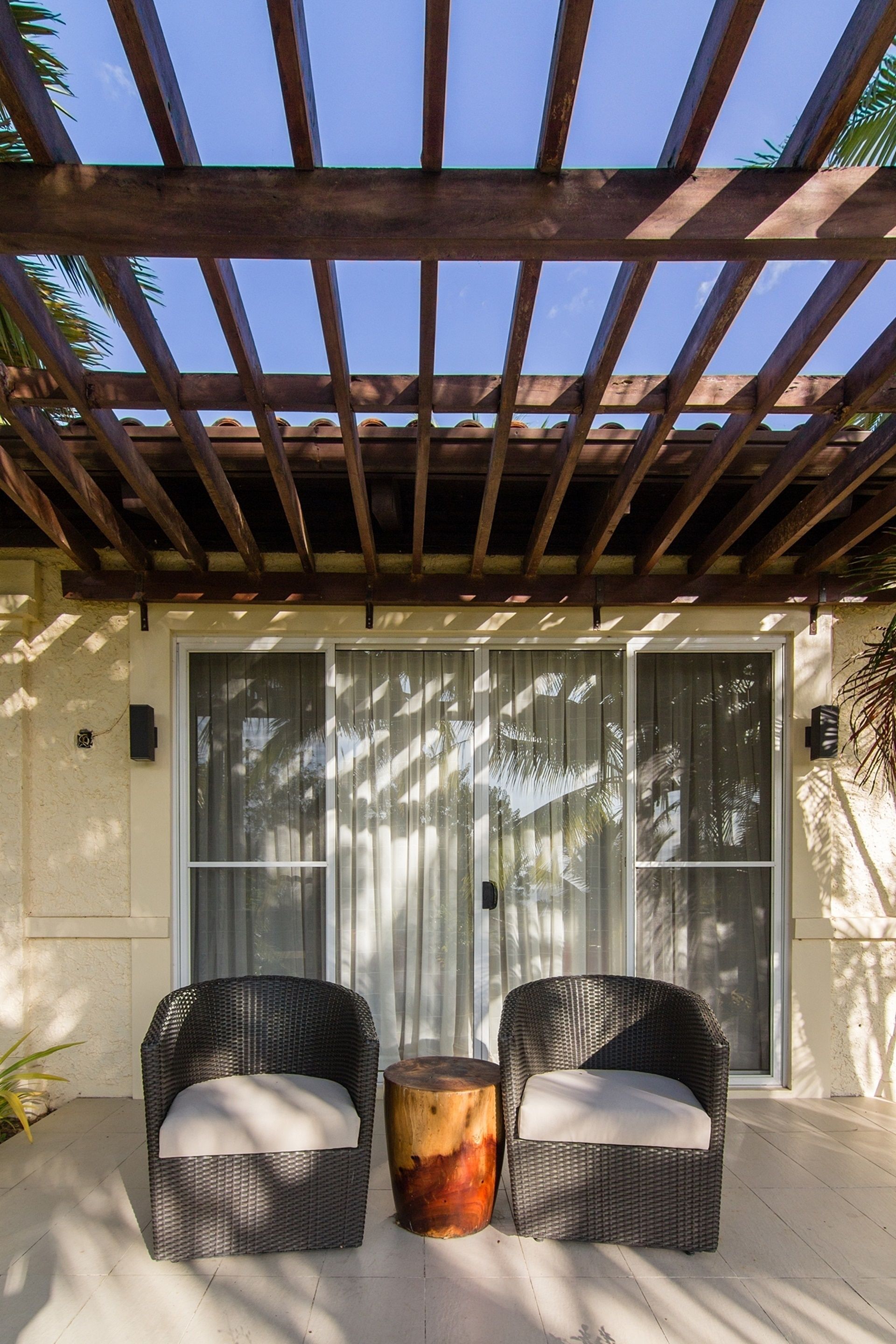 A covered patio area with two wicker chairs and a wooden table.