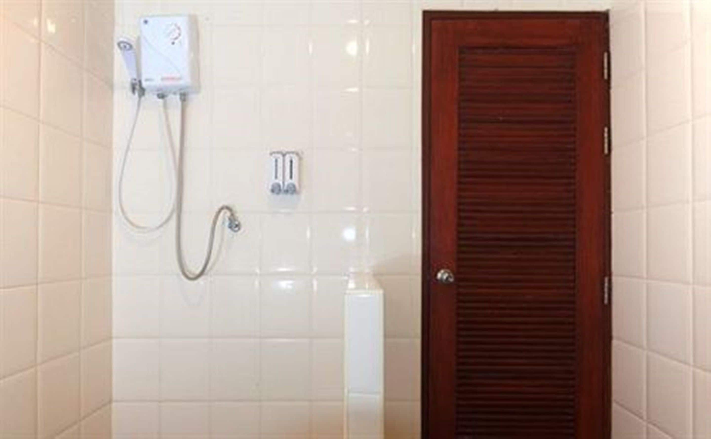 Un baño con paredes de azulejos blancos, una puerta de madera y una cabina de ducha con panel de control.