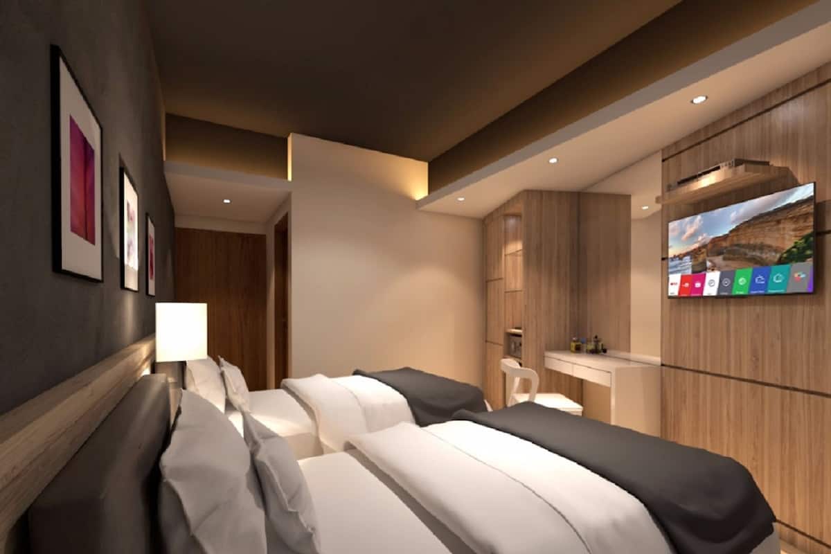 A modern hotel room with two beds, a TV on the wall, and a wooden wardrobe.