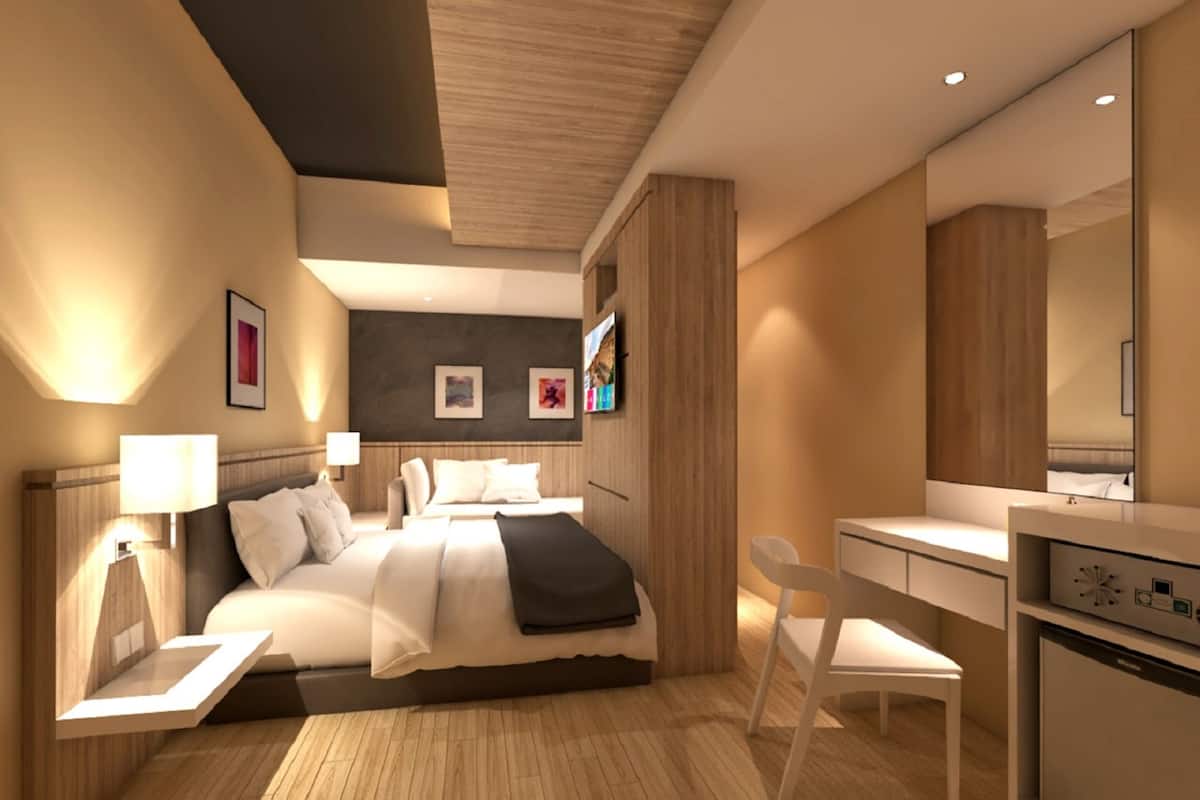 A modern hotel room with a bed, bedside table, chair, desk, and a built-in mini-fridge.