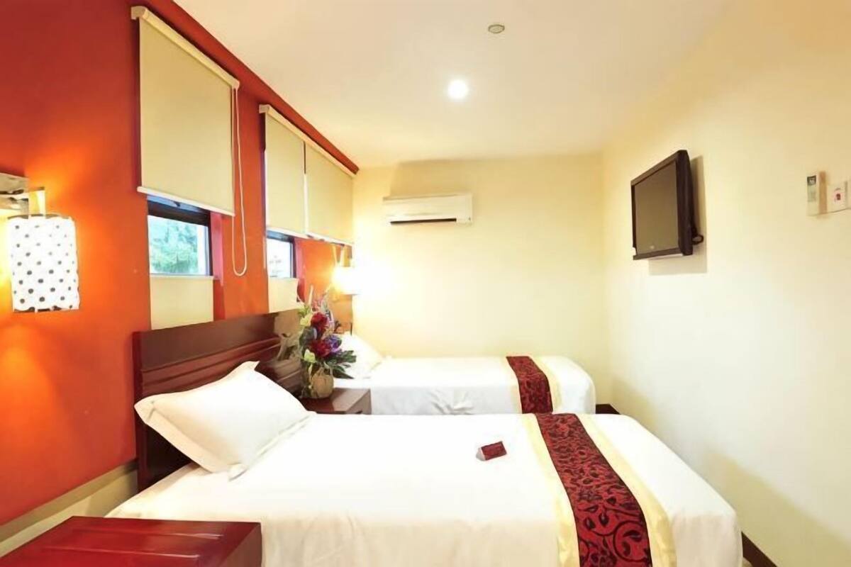 A hotel room with two beds, a large mirror, an air conditioning unit, and a television.
