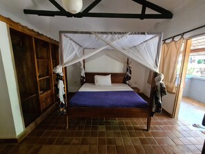 A room with a bed under a white canopy, wooden wardrobe, and a tiled floor. - Honey Badger Lodge (Moshi)