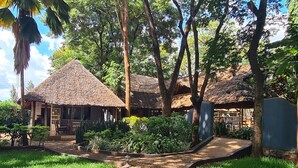 A thatched-roof building with a paved pathway leading to it, surrounded by lush greenery and trees. - Honey Badger Lodge (Moshi)