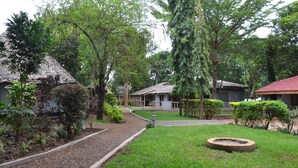 A courtyard with a gravel path, a circular stone feature, and several buildings with thatched roofs surrounded by lush greenery. - Honey Badger Lodge (Moshi)