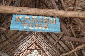 A rustic thatched roof structure with a wooden sign reading "KARIBU TENA". - Honey Badger Lodge (Moshi)